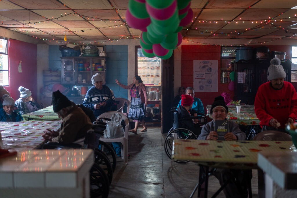 Personas mayores del hogar de ancianos en San Juan Comalapa, permanecen sentados en el comedor a la espera de su almuerzo. Foto/Edwin Bercián.
