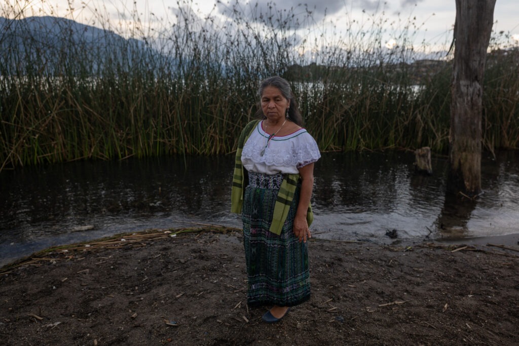 Flora Virginia Samuel González, integrante de las Guardianas del Lago, de pie en la orilla del Lago de Atitlán, San Pedro La Laguna, rodeada de vegetación acuática.
Foto: Edwin Bercián.