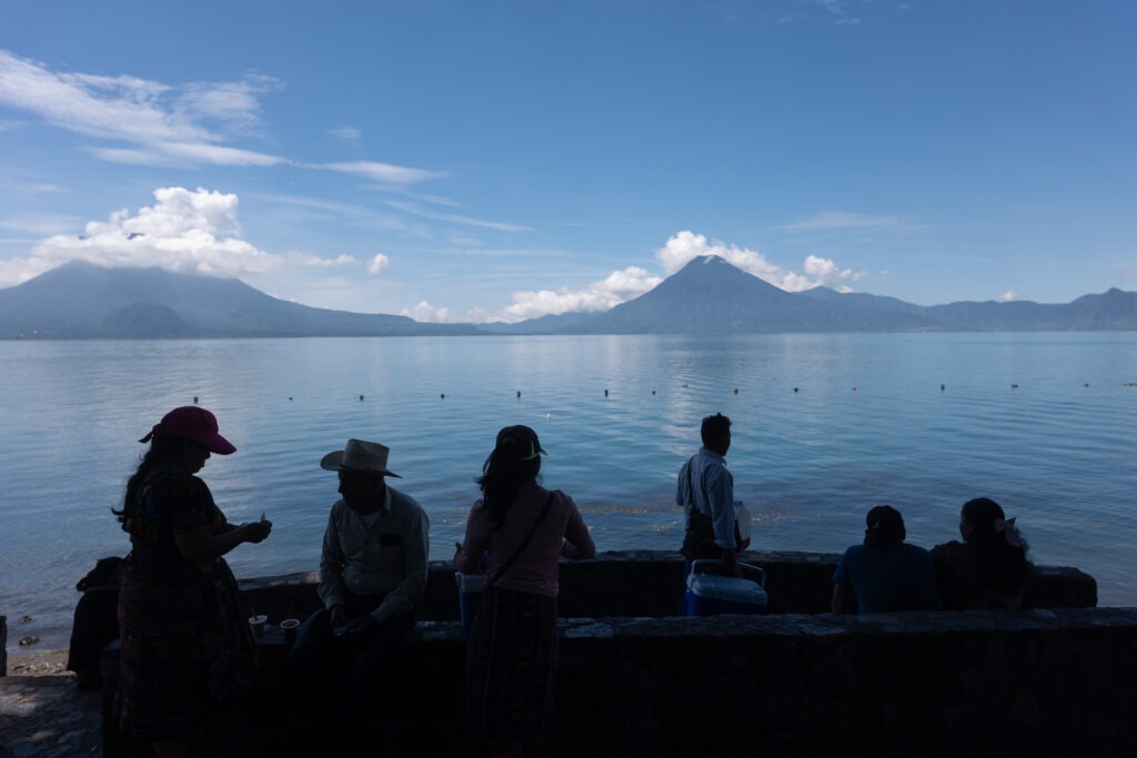 Personas de la comunidad de San Pedro La Laguna observan el Lago de Atitlán, con los volcanes al fondo, en una escena cotidiana vinculada a la vida comunitaria y al entorno natural. Foto: Edwin Bercián.