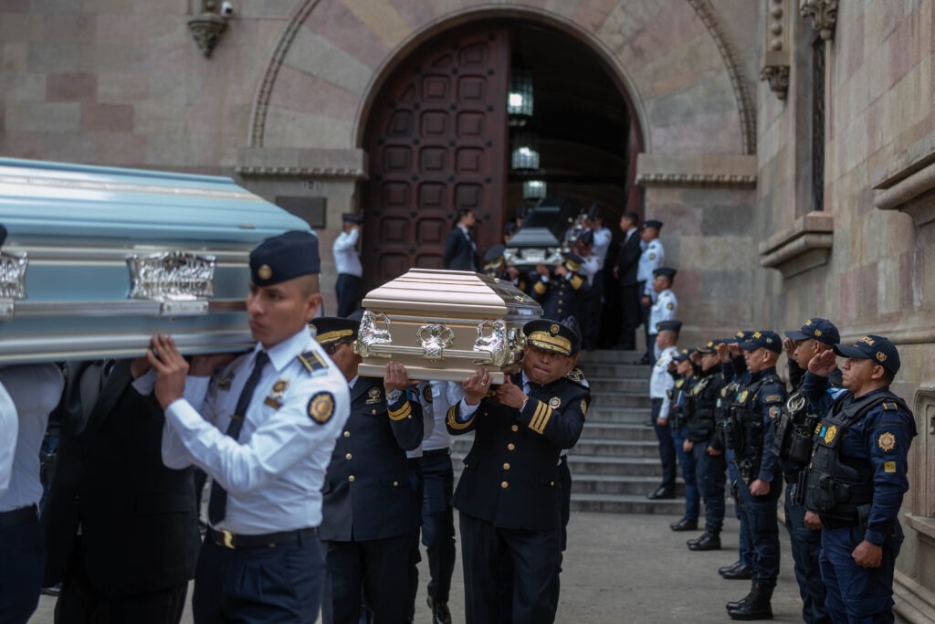 Pie de foto: Agentes de la Policía Nacional Civil trasladan los féretros de policías fallecidos durante un acto fúnebre realizado el 18 de enero de 2026, en la Ciudad de Guatemala, luego de los ataques del sábado 17 atribuidos a pandillas. Foto/Edwin Bercián. 

