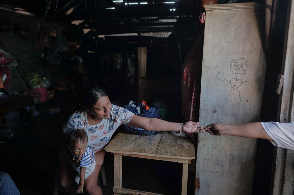 Mientras Darlin María Vicente sostiene a su hijo Ian con un brazo, con el otro recibe una moneda de un cliente por la compra de un dulce en su venta improvisada frente a la casa de sus suegros.