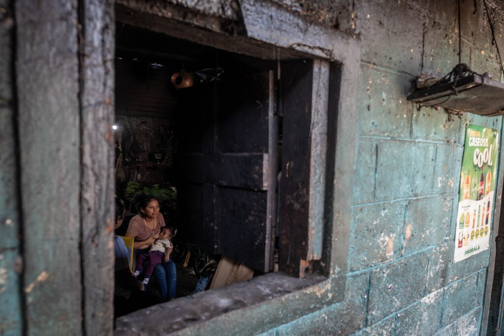 Sentada en una silla y viendo hacia la calle, Lesly Aracely Colop de 23 años, da pecho a su hijo Thiago Colop, de un año, en el vecindario de Parinox, en San Sebastián, Retalhuleu. Foto: Edwin Bercián